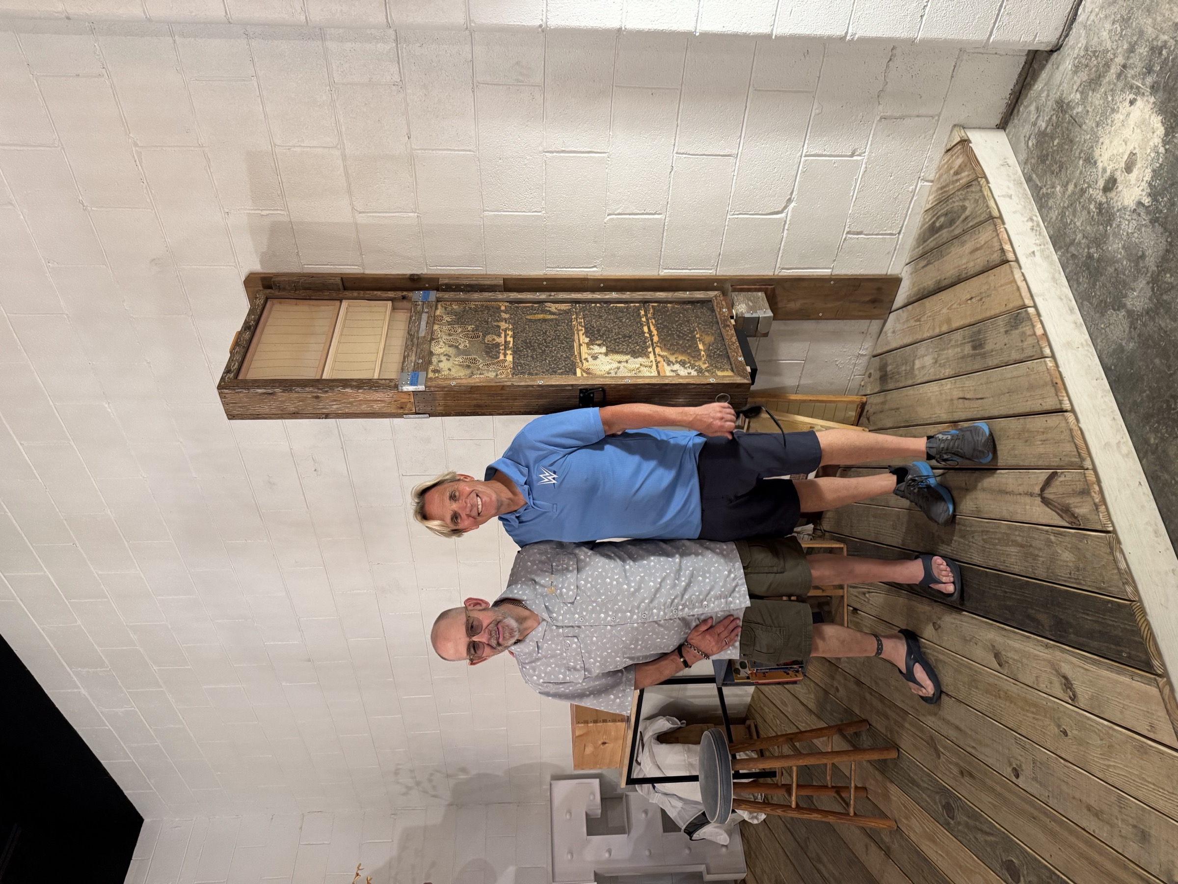 Charles Robinson and Kip Lee at Savannah Bee Company across from Enmarket Arena, August 2026, with an observation beehive on the wall behind them